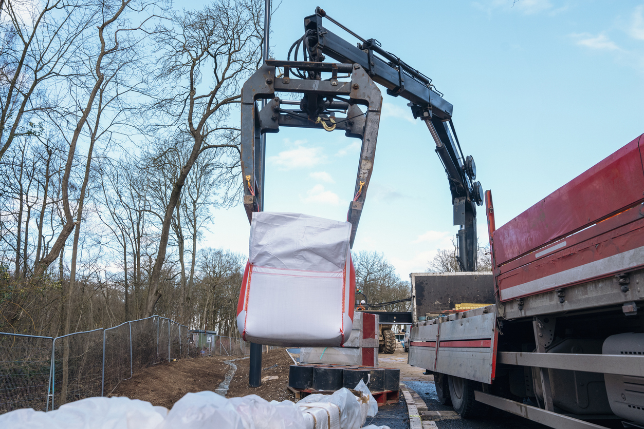 Lorry mounted crane lifting white bag